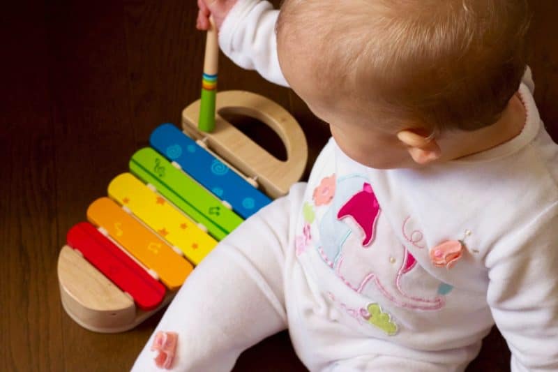 Baby plays with colored rainbow xylophone made of wood and metal