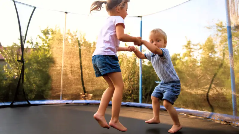 Two children jump together on a trampoline